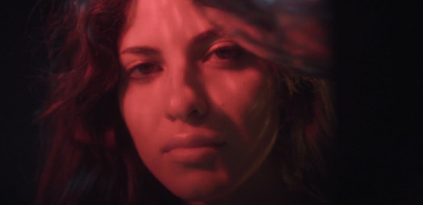 A woman's face lit in pink and teal against a mosaic of mirrored tiles (4/9)