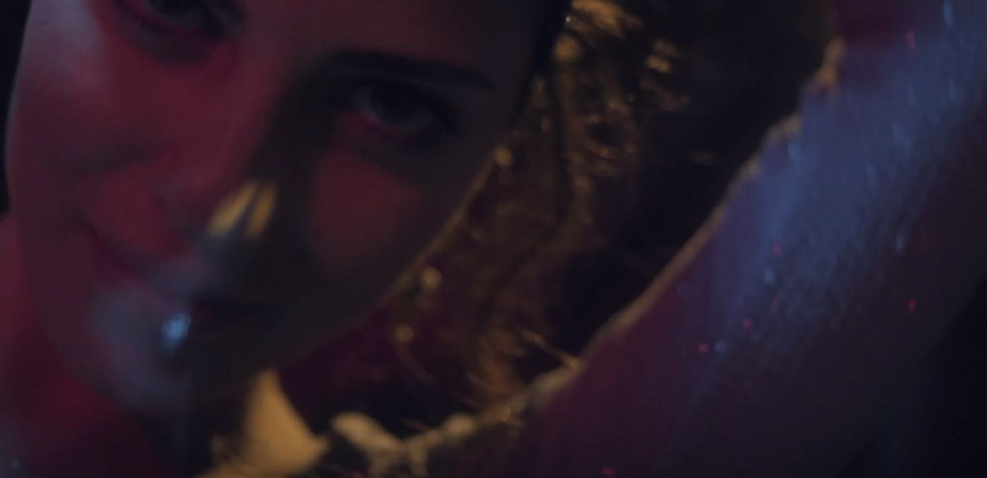 A woman's face lit in pink and teal against a mosaic of mirrored tiles (5/9)