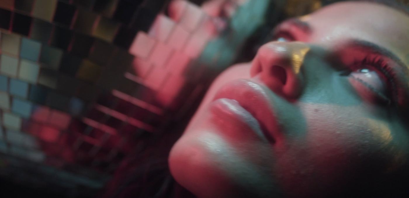 A woman's face lit in pink and teal against a mosaic of mirrored tiles (6/9)