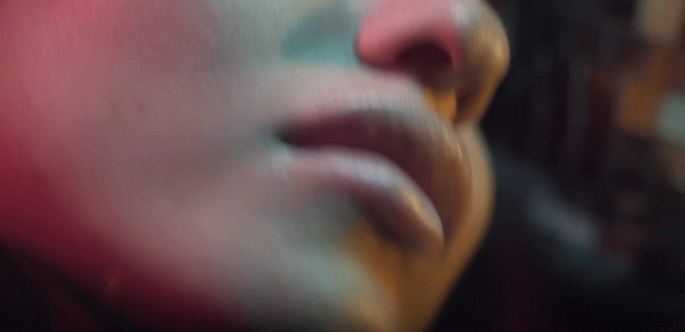 A woman's face lit in pink and teal against a mosaic of mirrored tiles (7/9)