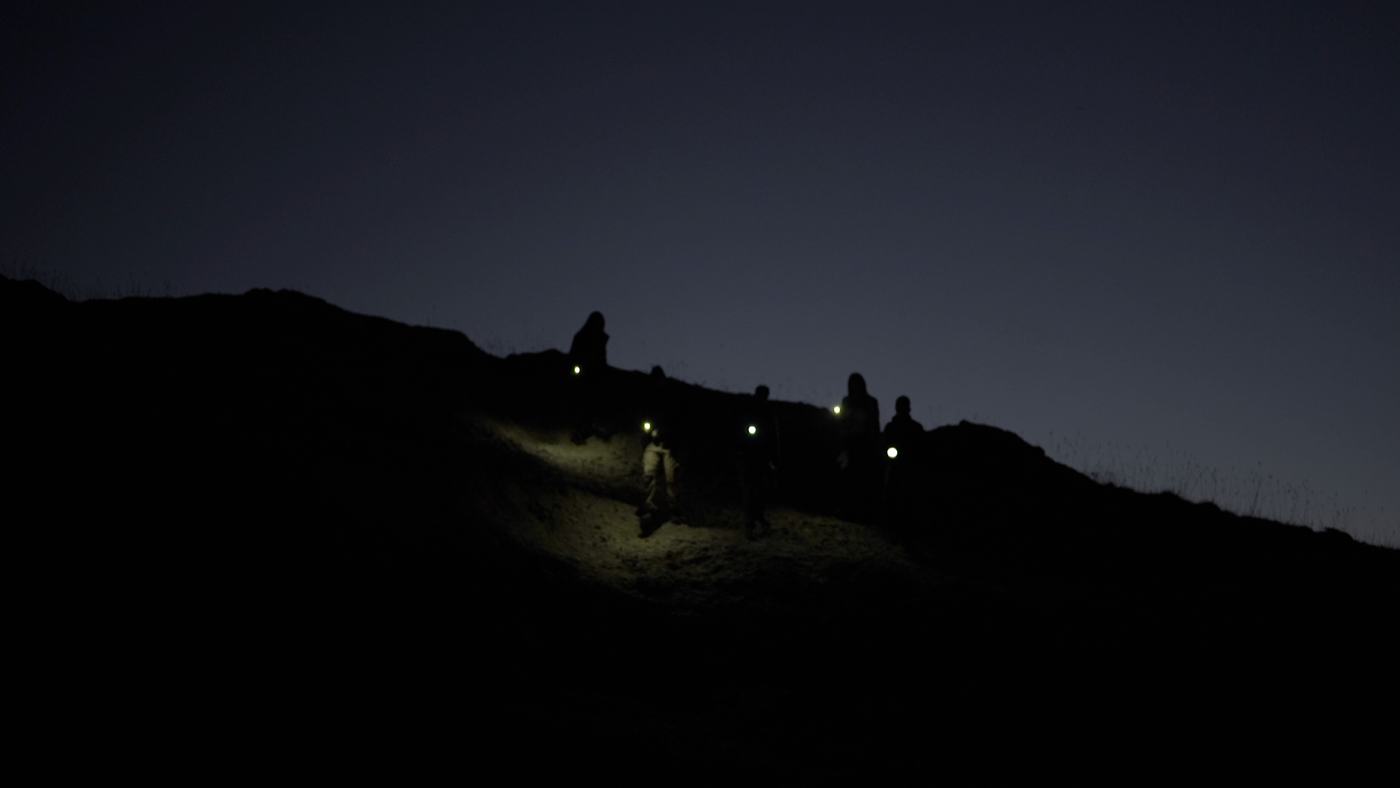 People gathered around a campfire at night on a mountainside (4/12)