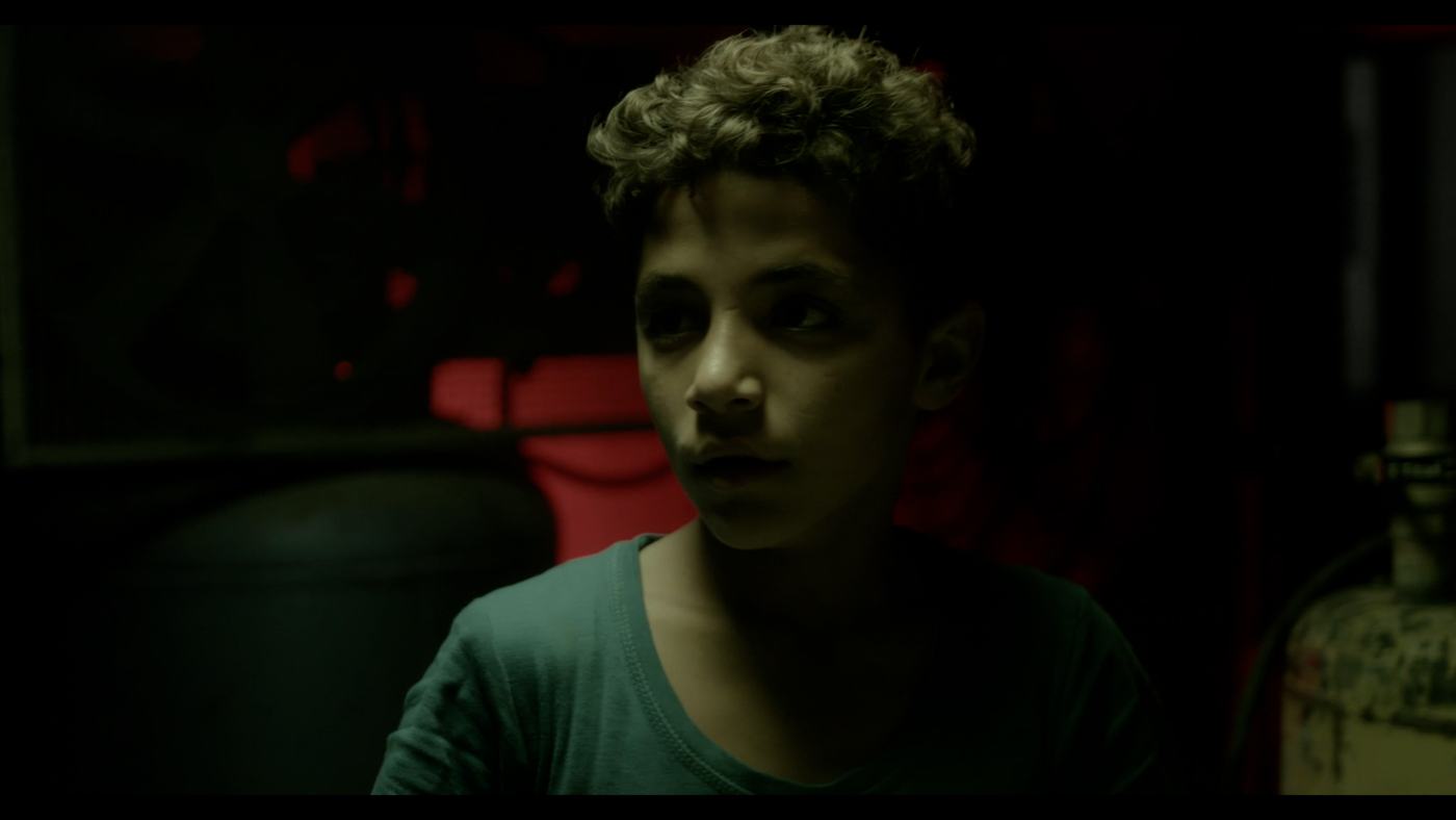 A boy in a blue shirt looks off-frame in a dim truck cab (9/12)