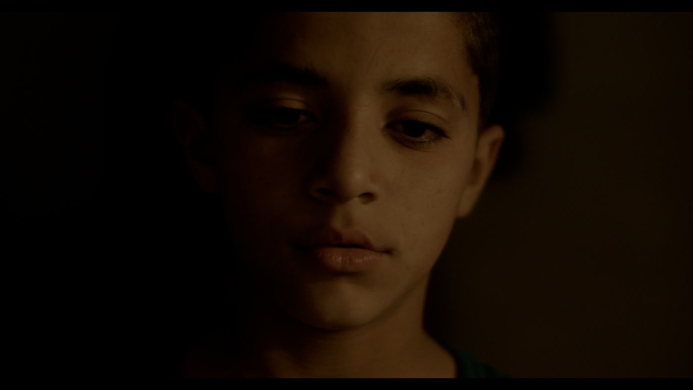 A boy in a blue shirt looks off-frame in a dim truck cab (12/12)