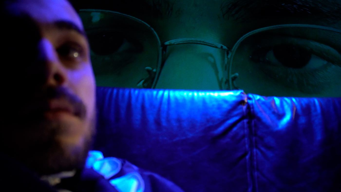 A man in blue and green light lies back, eyes open (9/15)