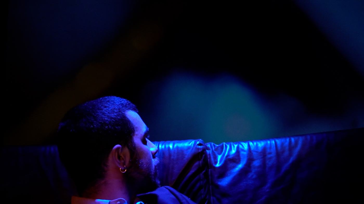 A man in blue and green light lies back, eyes open (10/15)