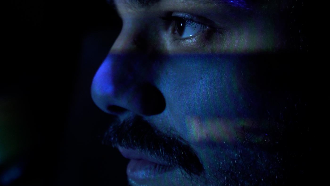 A man in blue and green light lies back, eyes open (11/15)